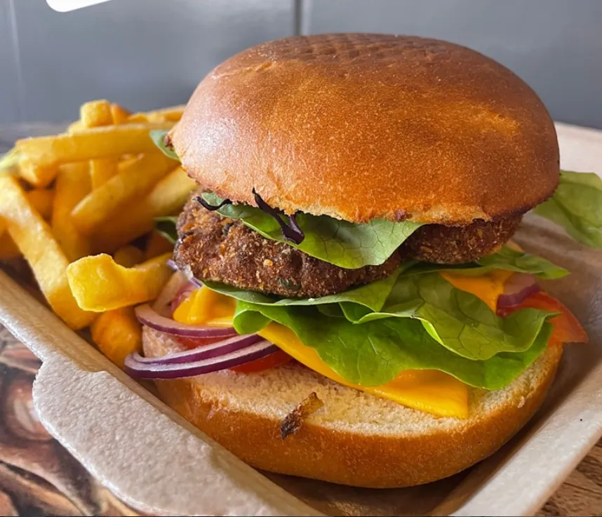 Un burger de Holy sur un plateau de bois : pain brioché doré, steak épais, cheddar fondu, salade et oignons rouges, avec une portion de frites maison à côté.